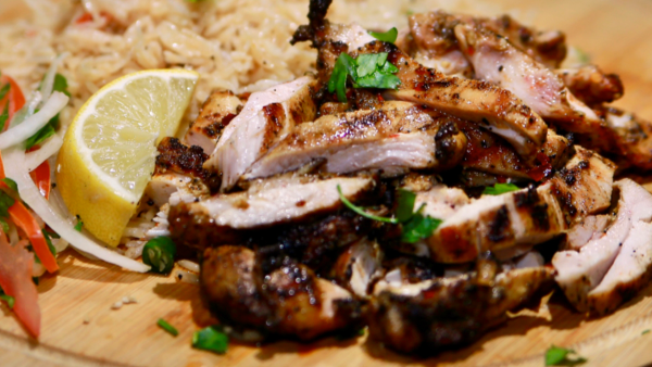 A bowl of spicy grilled boneless chicken sliced over seasoned rice with a small salad on the side